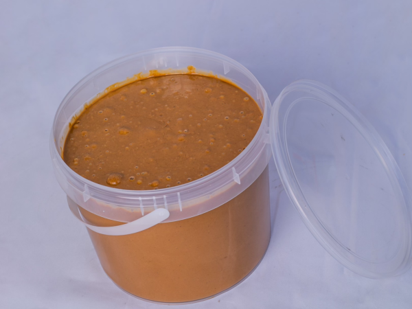 Seau ouvert de 5 litres de pâte d'arachide 'Saveur d'Afrique', révélant le produit 100% naturel, sur un fond uni.