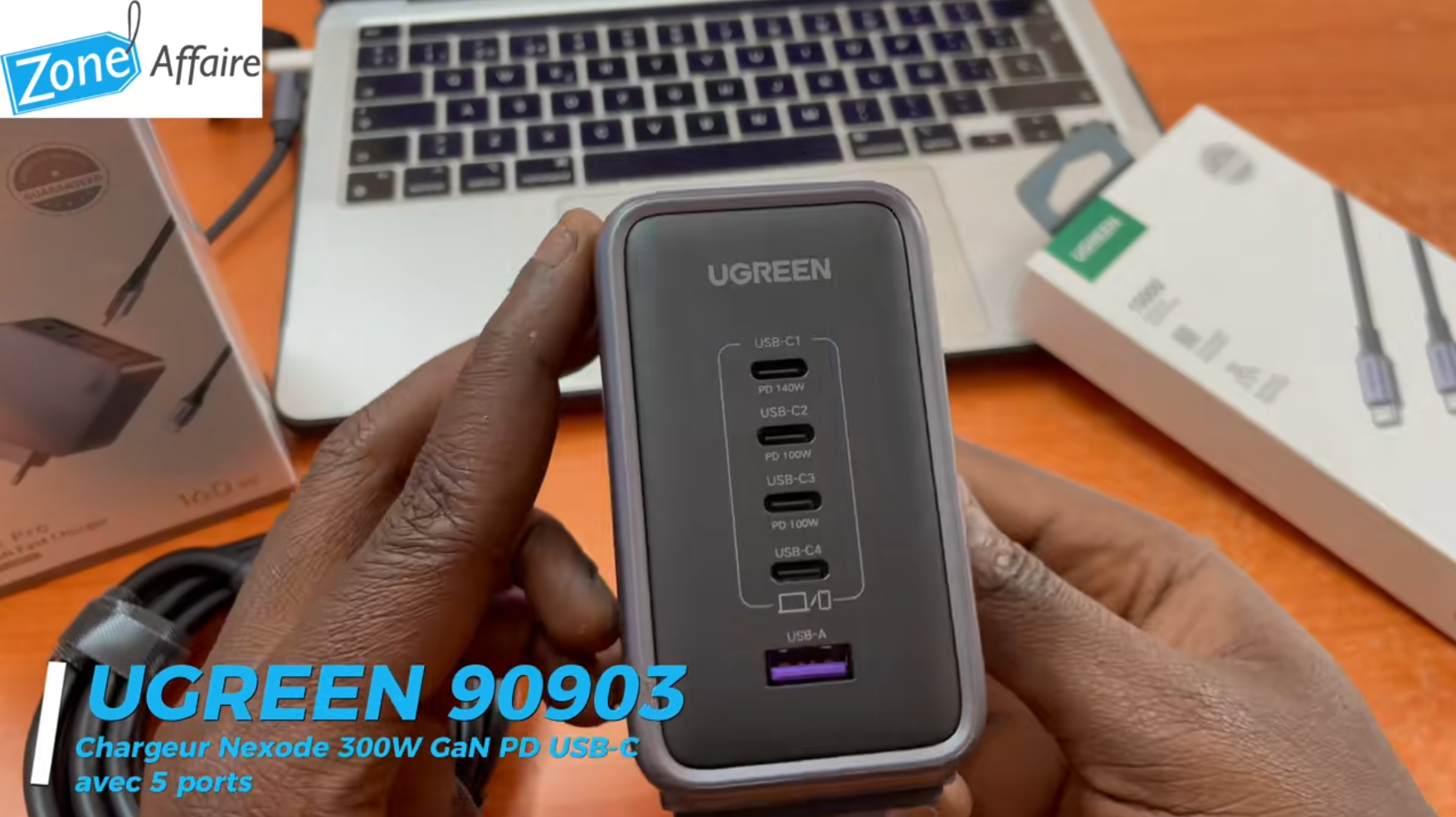 Chargeur UGREEN Nexode 300W avec ports USB-C et USB-A tenu en main devant un ordinateur portable.